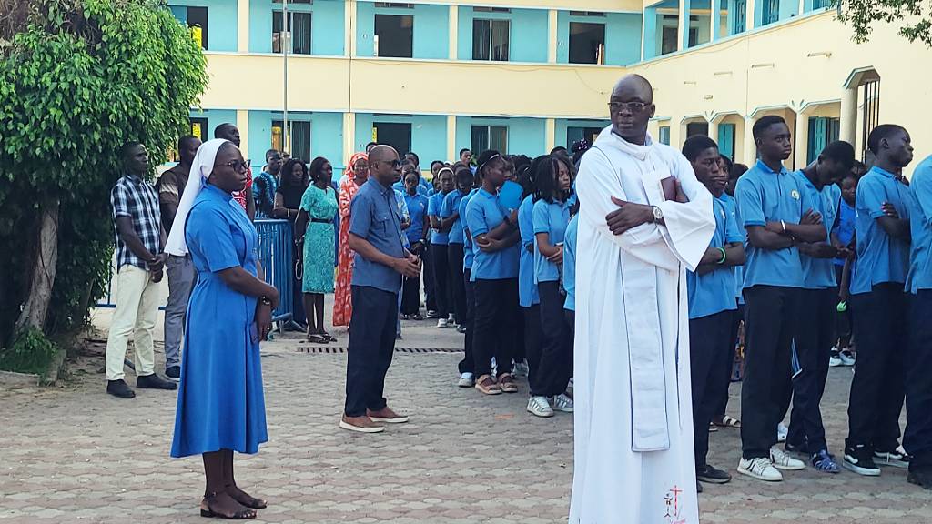 Le Père Abraham, Sœur Rosalie, les enseignants et les apprenants de l’AMJ marquent une halte de prière dans la cour de l’école au cours d’une marche spirituelle empreinte de foi et de recueillement.
